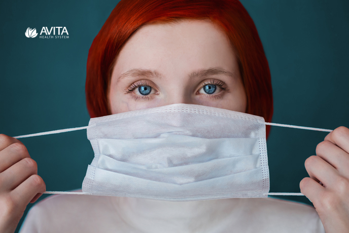 woman with red hair holding surgical mask in front of face